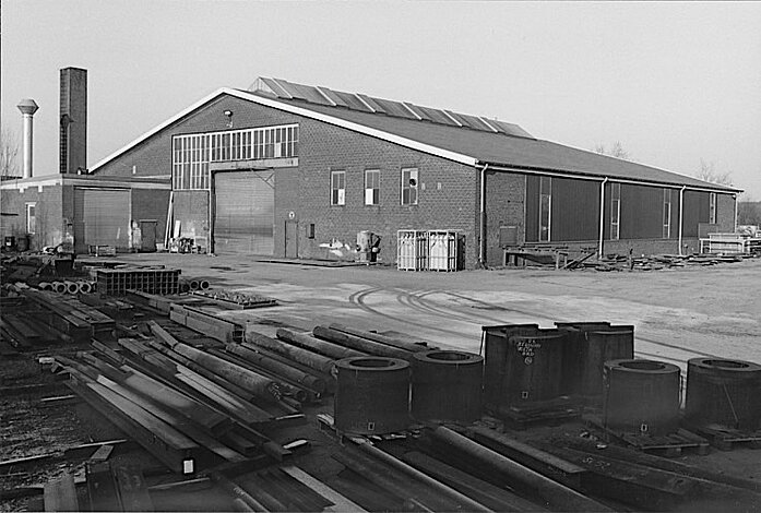 Schwarz-Weiß-Foto der Grenzlandhalle in Borken. Vor der Halle liegen Stahlelemente auf dem Gelände.